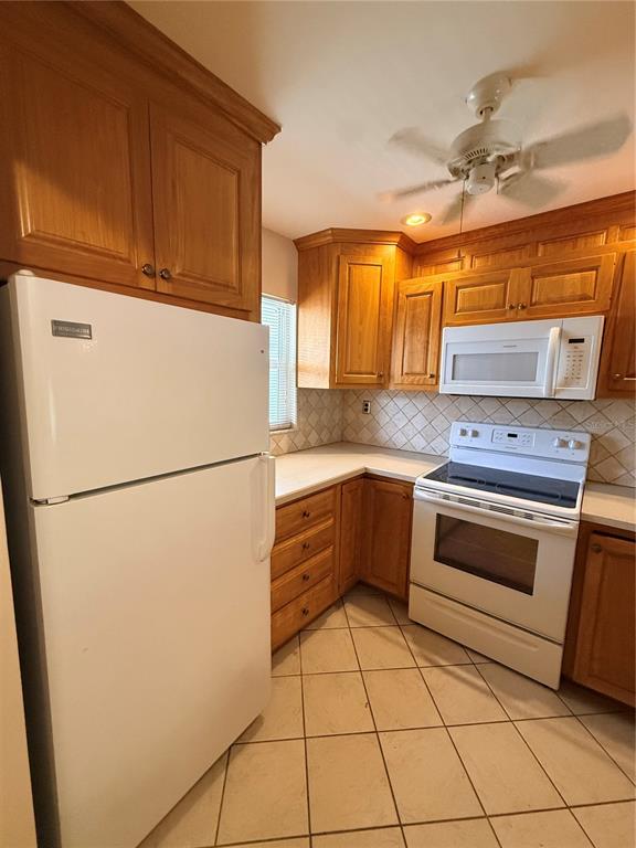 A kitchen with wood cabinets, white appliances, and light-colored tile flooring — 100 E KENTUCKY AVENUE UNIT A106, DELAND, FL