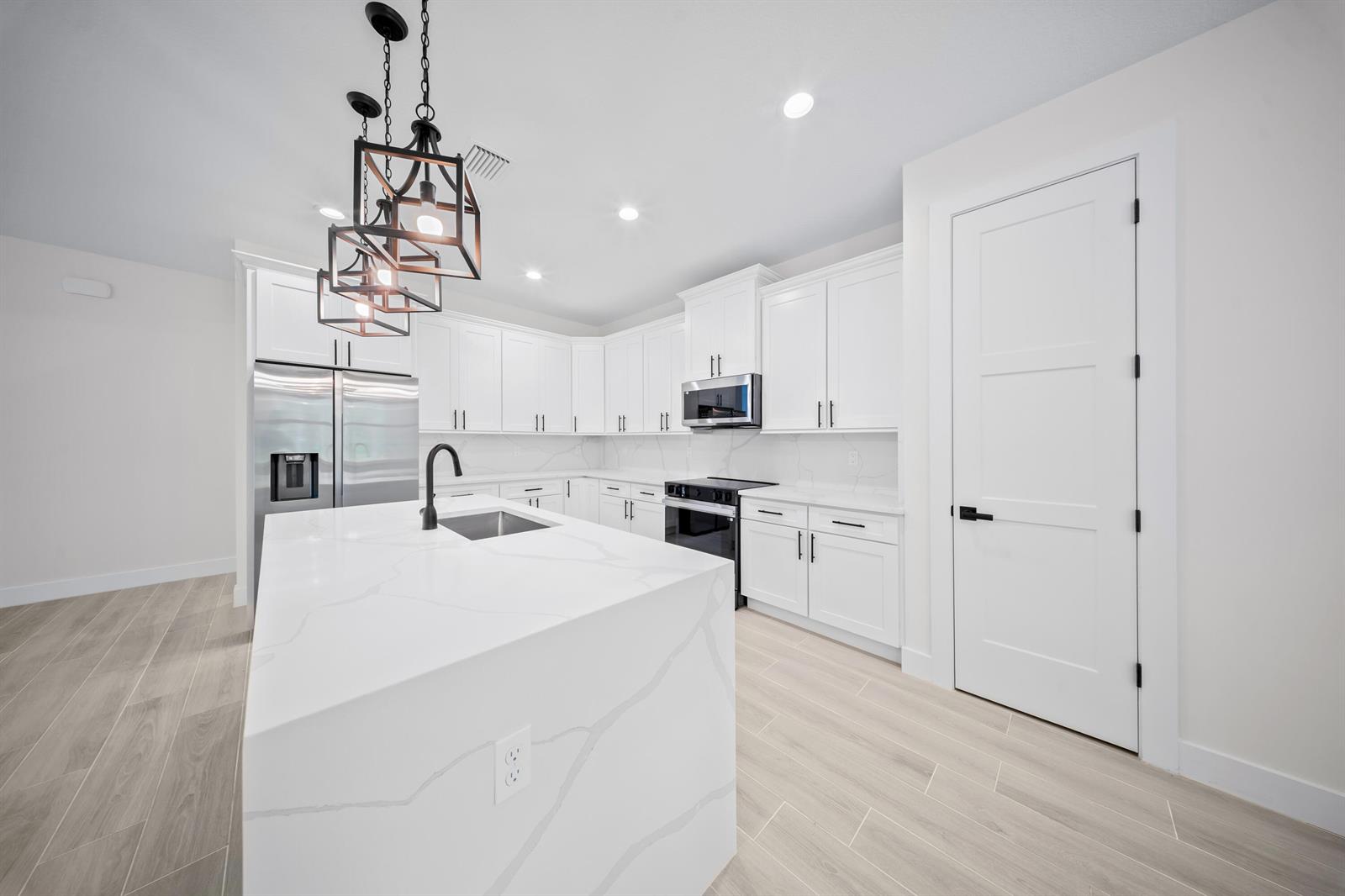A modern kitchen features white cabinetry, a marble-topped island, stainless steel appliances, and wood-look flooring — 17521 N 76th St Street N, FL 33470, FL