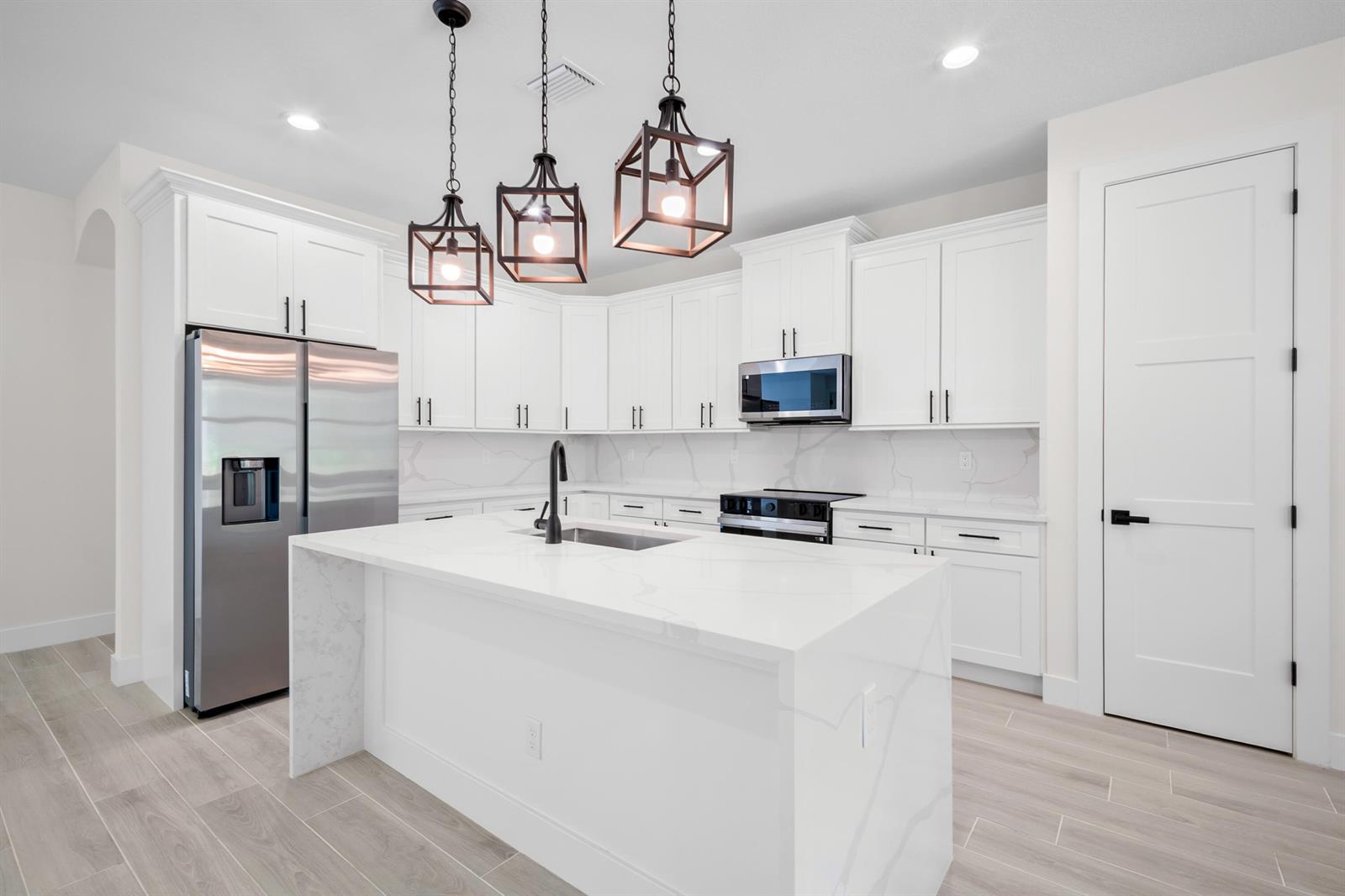 A modern kitchen features white cabinets, a marble-topped island, stainless steel appliances, and pendant lighting — 17521 N 76th St Street N, FL 33470, FL