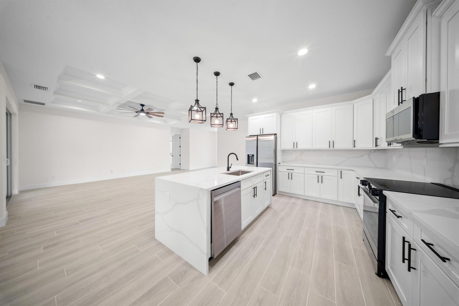 A modern kitchen features white cabinets, a quartz island, and light wood-look tile flooring — 17521 N 76th St Street N, FL 33470, FL
