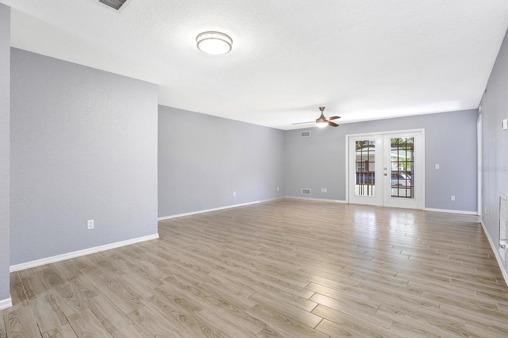An empty living room features light gray walls, wood-look flooring, a ceiling fan, and French doors — 107 47TH AVENUE N, ST PETERSBURG, FL
