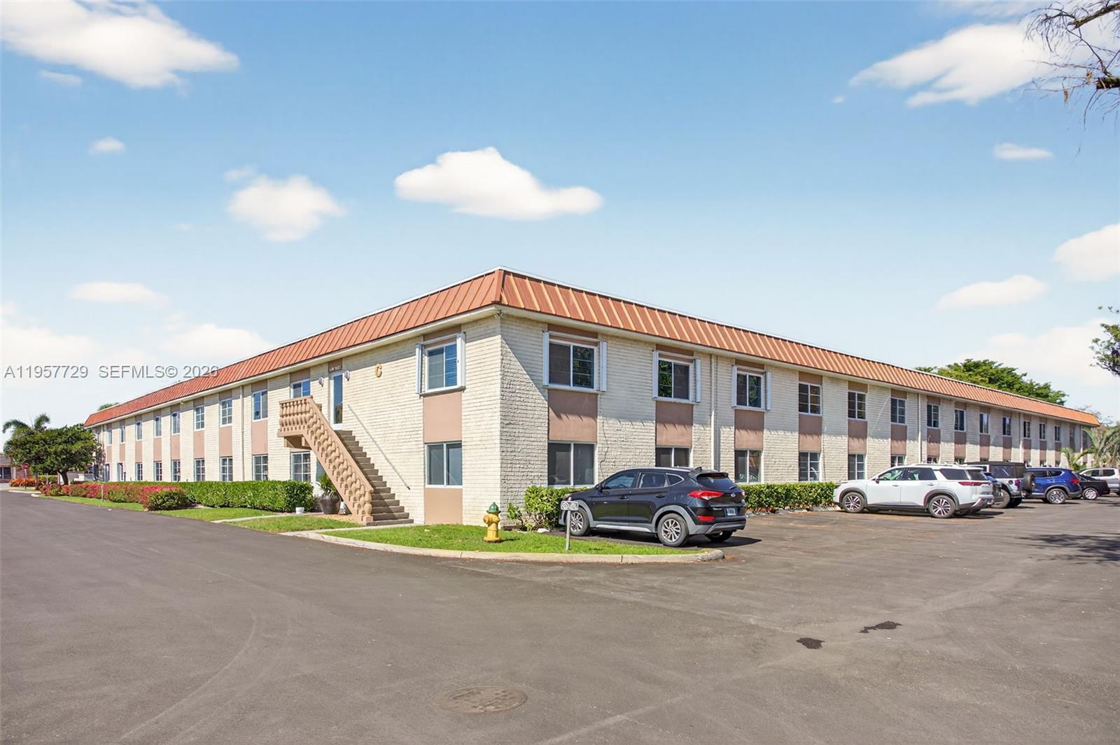 A two-story apartment building with a brick exterior and a metal roof sits beside a parking lot — 9 NE 19th Ct # 104C, Wilton Manors FL 33305, WILTON MANORS, FL