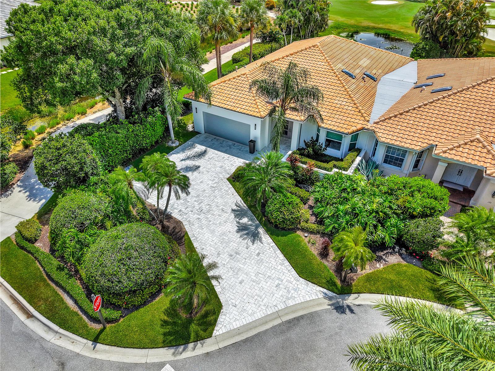 An aerial view of a house with a tiled roof, paver driveway, and lush landscaping — 124 Golf Village Boulevard, Jupiter FL 33458, JUPITER, FL