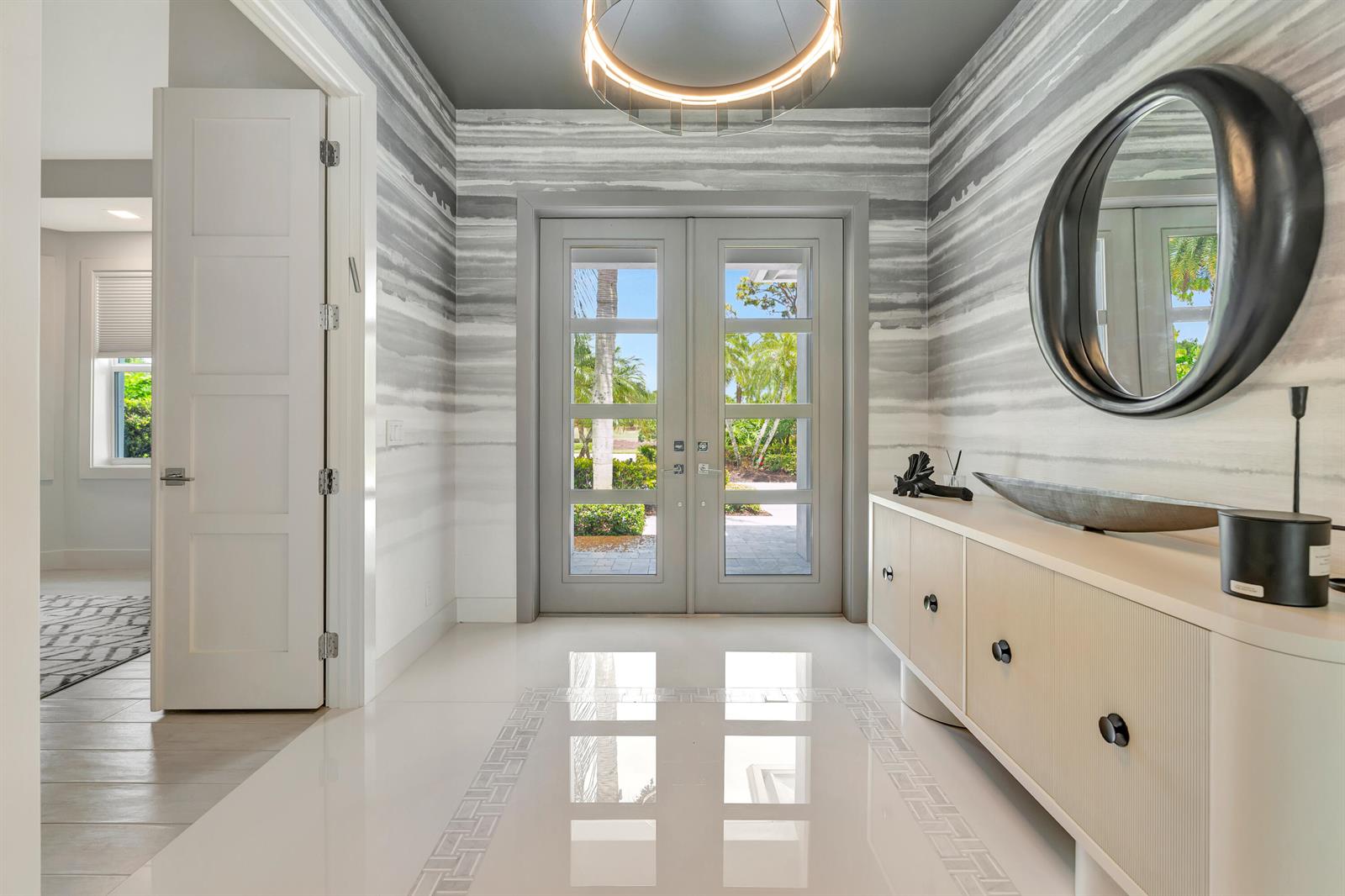A modern entryway features horizontal striped wallpaper, a circular mirror, and a light-colored console table — 124 Golf Village Boulevard, Jupiter FL 33458, JUPITER, FL