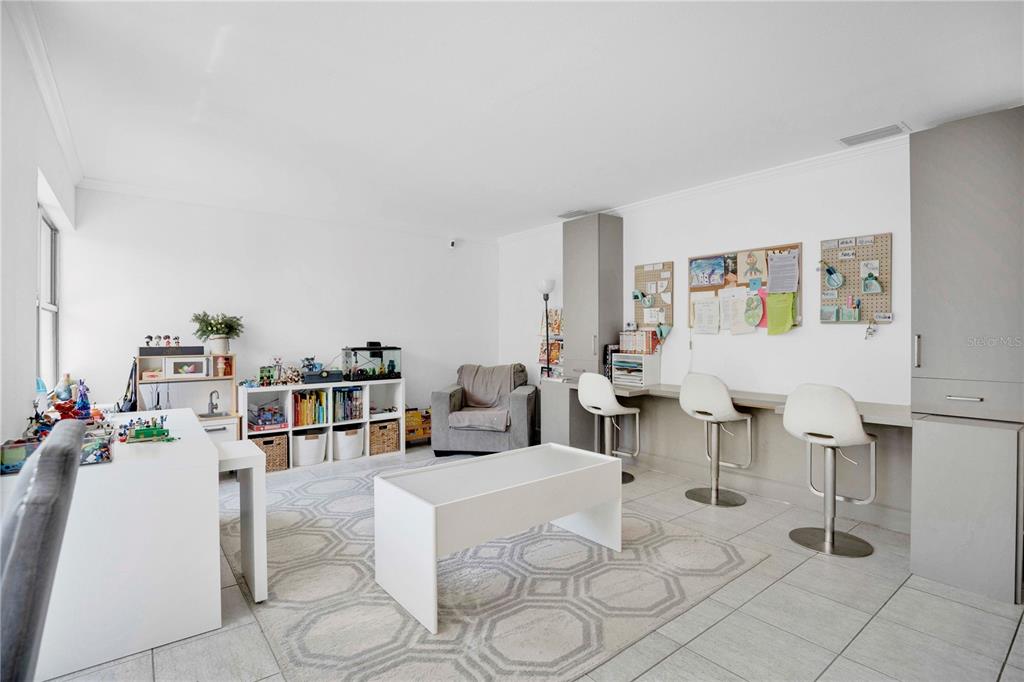 A bright playroom features a long built-in desk, white shelving, and a patterned area rug — 7207 GREENVILLE COURT, ORLANDO, FL