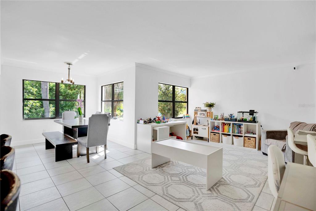 A bright, open-concept dining and living area features white walls, tile floors, and large windows — 7207 GREENVILLE COURT, ORLANDO, FL