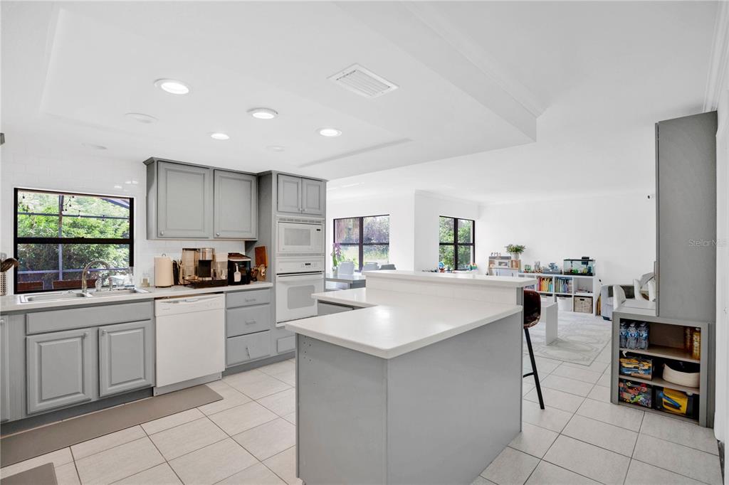 A kitchen with gray cabinets, white countertops, and tile flooring opens into a living area — 7207 GREENVILLE COURT, ORLANDO, FL