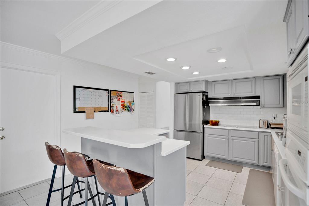 A kitchen features gray cabinets, stainless steel appliances, a white breakfast bar, and tile flooring — 7207 GREENVILLE COURT, ORLANDO, FL