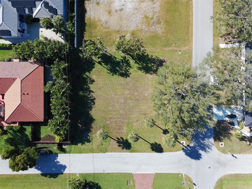 An aerial view shows a vacant, grassy residential lot situated between two houses and a street — 702 HIBISCUS DRIVE, VENICE, FL