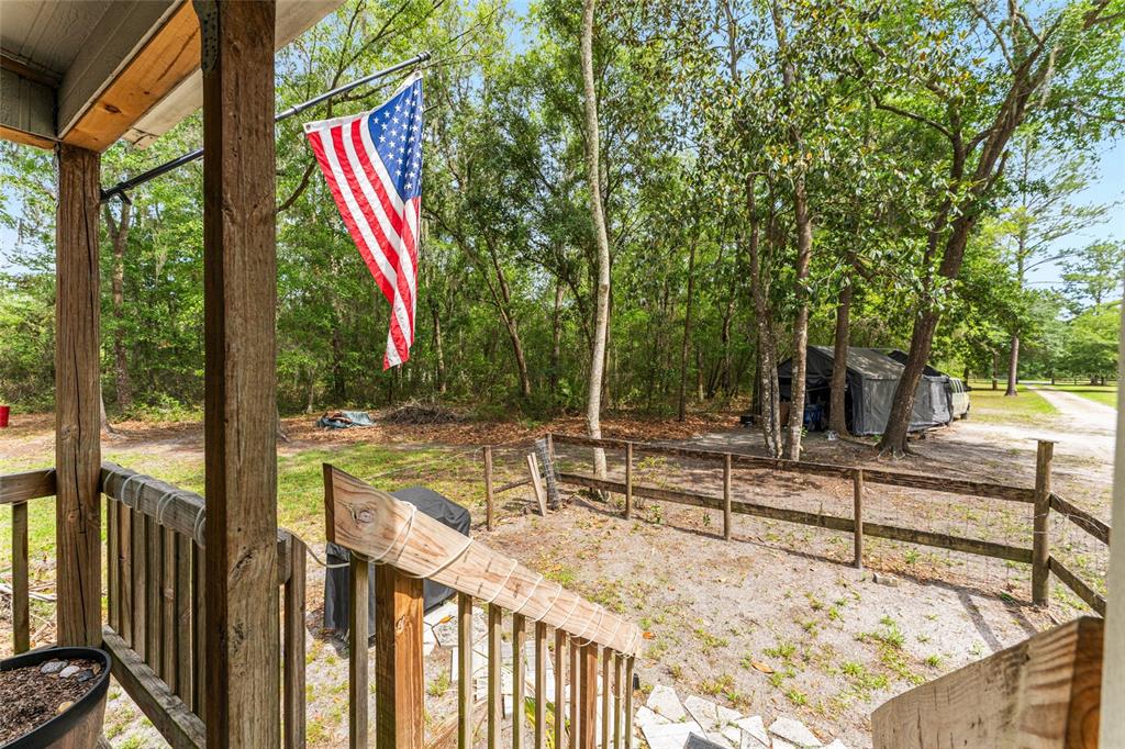 A wooden porch overlooks a sandy yard with a fence, trees, and a covered structure — 1504 NW 156TH AVENUE, GAINESVILLE, FL