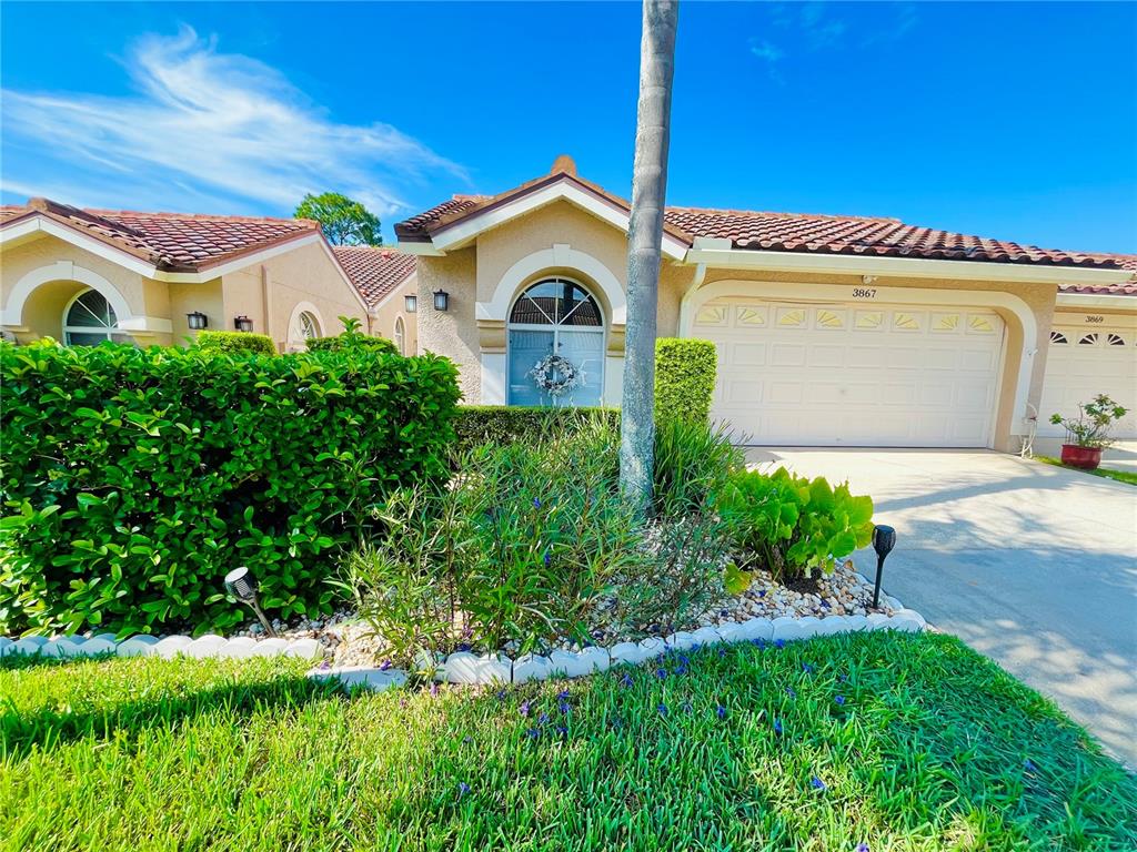 A single-story house exterior with a tiled roof, beige stucco walls, and a landscaped front yard — 3867 DARSTON STREET, PALM HARBOR, FL