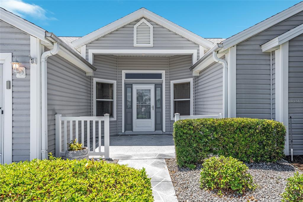 The exterior of a gray-sided house features a covered entryway with a white front door — 170 PALERMO PLACE, LADY LAKE, FL