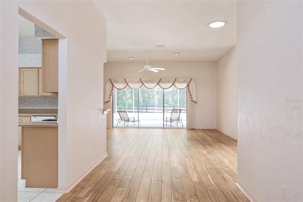 A view from a tiled kitchen into a living area with wood-look flooring and sliding doors — 170 PALERMO PLACE, LADY LAKE, FL