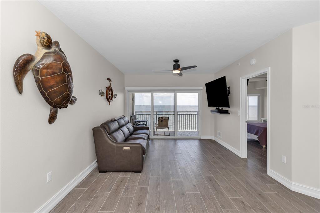 A living room features wood-look tile flooring, a leather sofa, and a balcony with ocean views — 1805 RIVERSIDE DRIVE UNIT 506, TITUSVILLE, FL