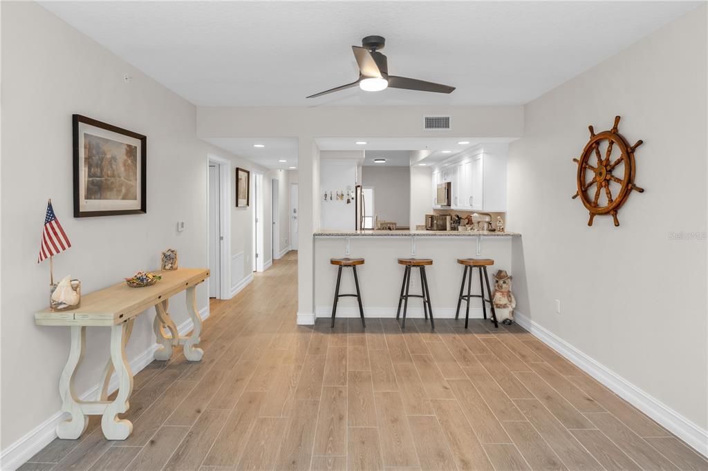 A room with light wood-look tile flooring, a breakfast bar with three stools, and a ceiling fan — 1805 RIVERSIDE DRIVE UNIT 506, TITUSVILLE, FL