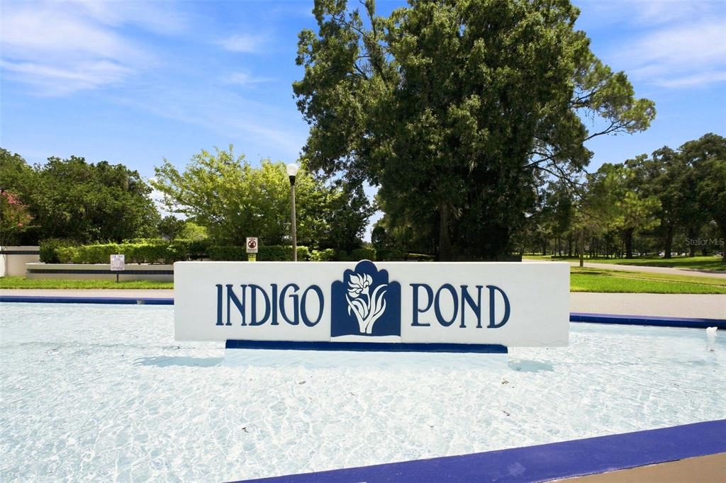 A sign for Indigo Pond stands in front of a shallow water feature outdoors — 3588 INDIGO POND DRIVE UNIT 12, PALM HARBOR, FL
