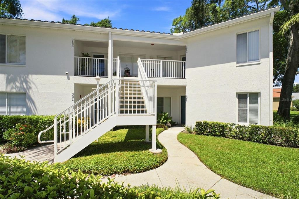 A two-story white apartment building features an exterior staircase leading to an upper-level balcony — 3588 INDIGO POND DRIVE UNIT 12, PALM HARBOR, FL