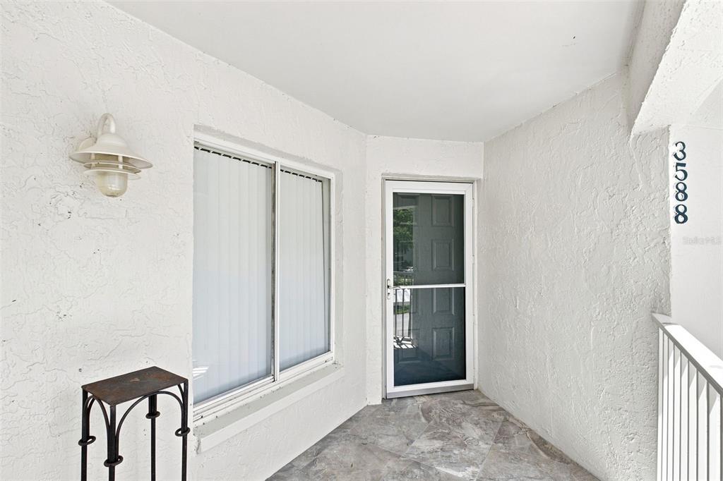 A white stucco entryway features a glass storm door, a window, and tiled flooring — 3588 INDIGO POND DRIVE UNIT 12, PALM HARBOR, FL