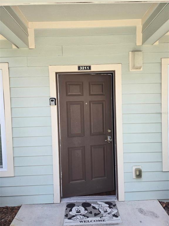 The exterior view shows a brown front door with a Mickey Mouse welcome mat — 3211 GOLD LANE, KISSIMMEE, FL