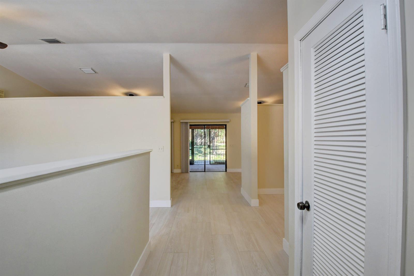 A hallway with light wood-look flooring leads toward a glass sliding door to a patio — 7011 San Sebastian Circle, Boca Raton FL 33433, BOCA RATON, FL
