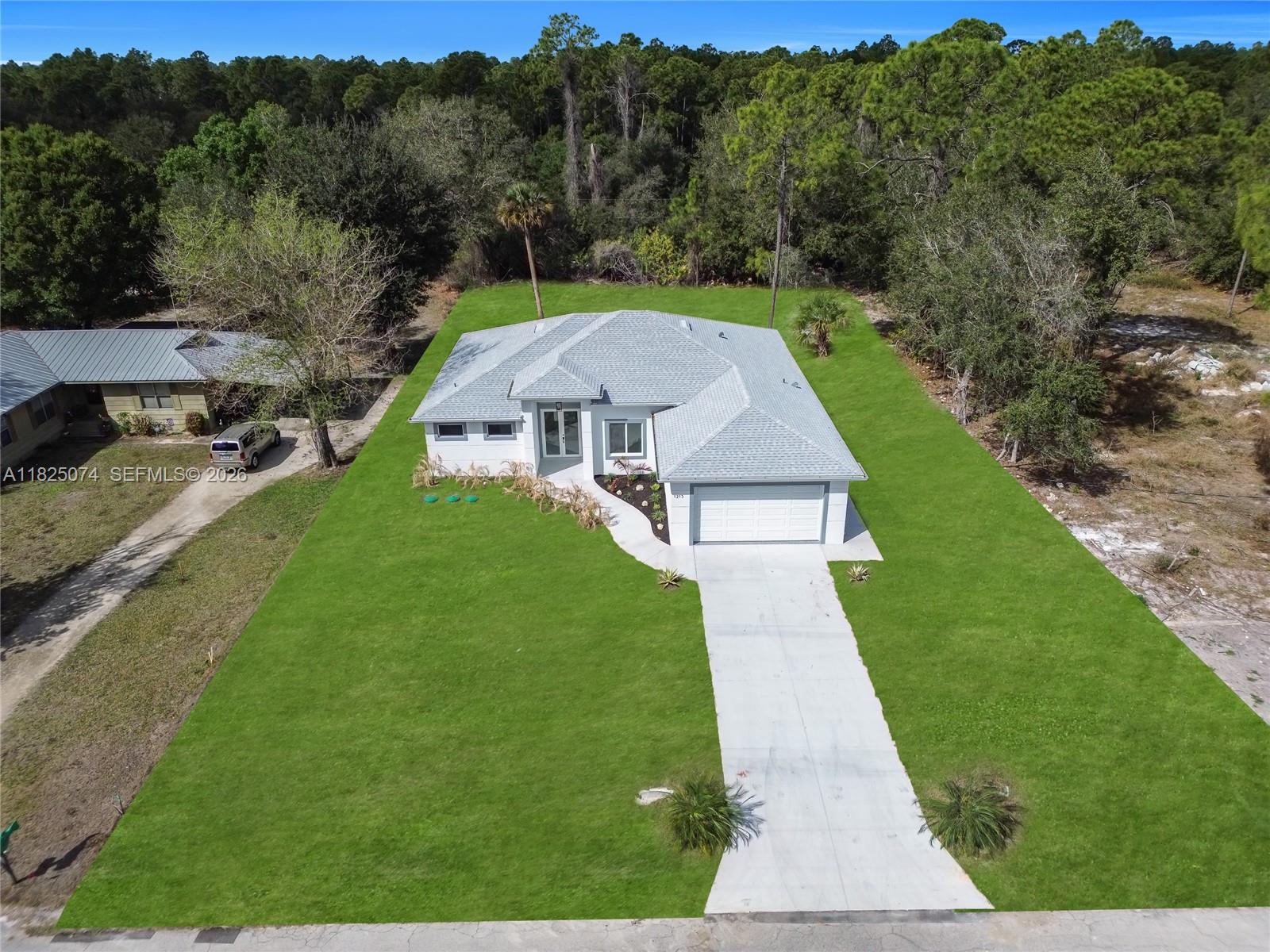 An aerial view shows a single-story house with a gray roof and a concrete driveway — 1215 Fitch Ave, Lehigh Acres FL 33972, LEHIGH ACRES, FL