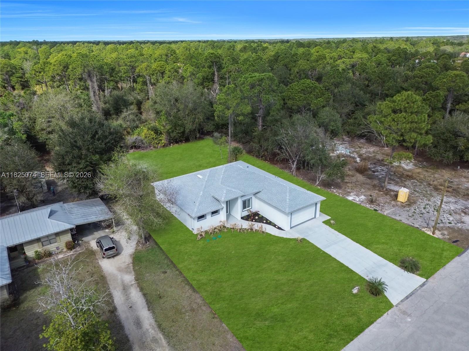 An aerial view shows a single-story house with a gray roof and a concrete driveway — 1215 Fitch Ave, Lehigh Acres FL 33972, LEHIGH ACRES, FL