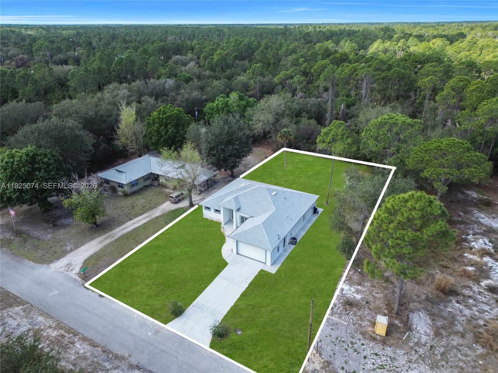 An aerial view shows a single-story house with a concrete driveway surrounded by wooded land — 1215 Fitch Ave, Lehigh Acres FL 33972, LEHIGH ACRES, FL