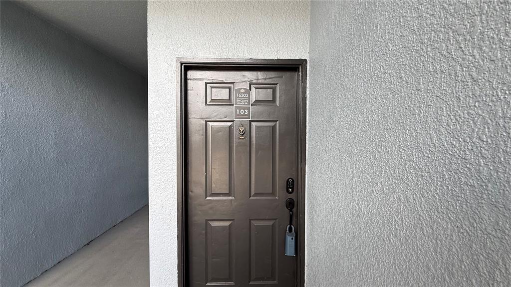 The exterior of a gray stucco apartment building features a unit number sign and stairwell — 16303 ENCLAVE VILLAGE DRIVE UNIT 103, TAMPA, FL