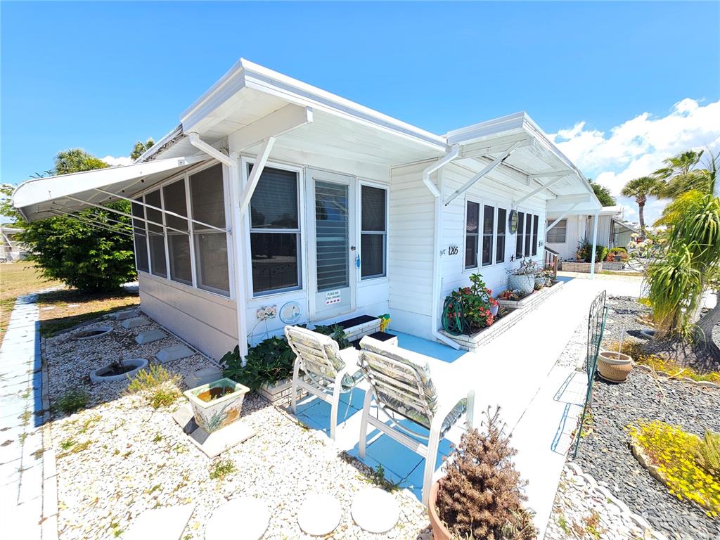 A white mobile home with a screened porch, outdoor seating, and a gravel yard — 205 VIA VENETO, VENICE, FL