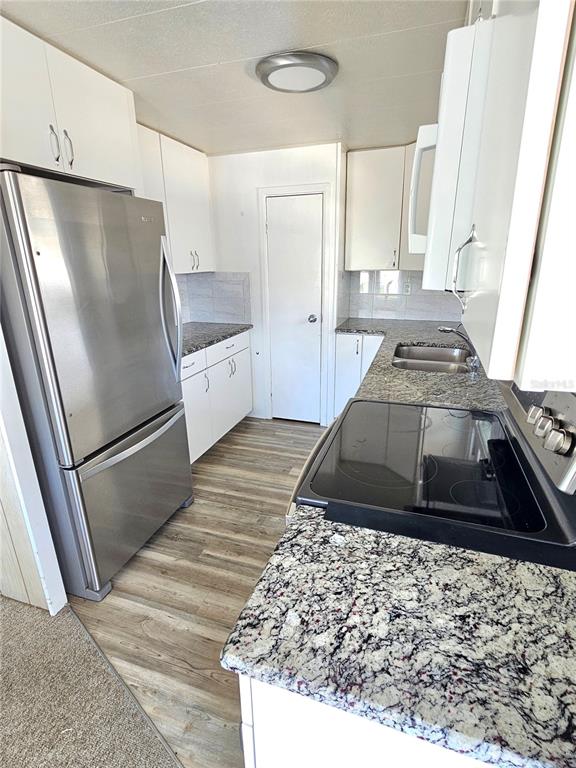 A kitchen features white cabinets, stainless steel appliances, granite countertops, and light wood-look flooring — 205 VIA VENETO, VENICE, FL