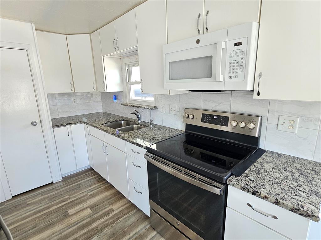A kitchen features white cabinets, granite countertops, a stainless steel stove, and wood-look flooring — 205 VIA VENETO, VENICE, FL