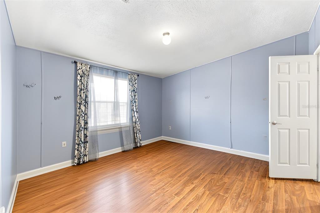 An empty bedroom features light blue walls, wood-look flooring, and a single window with curtains — 4313 ORLANDO AVENUE, BROOKSVILLE, FL