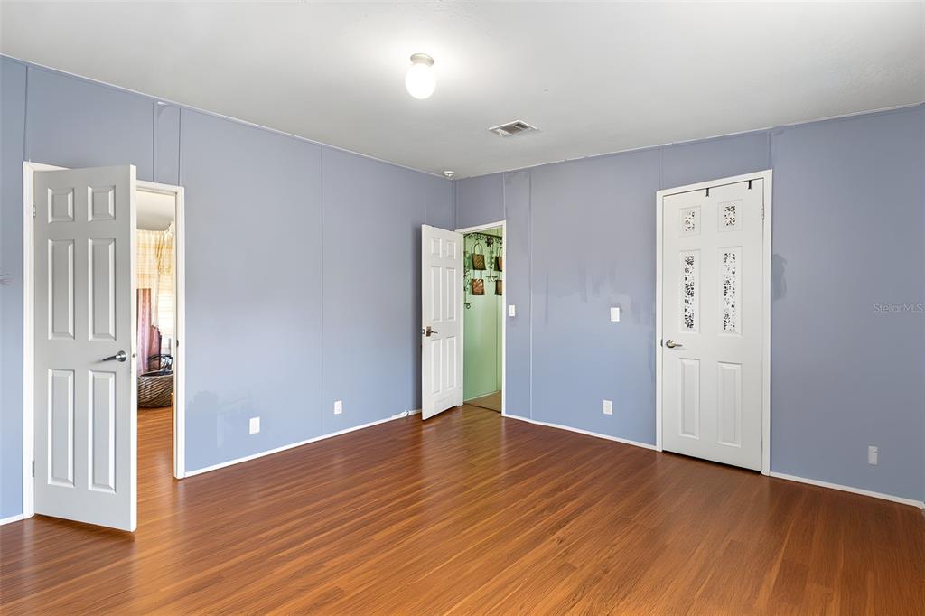 A bedroom with blue walls, wood-look flooring, and three white doors — 4313 ORLANDO AVENUE, BROOKSVILLE, FL