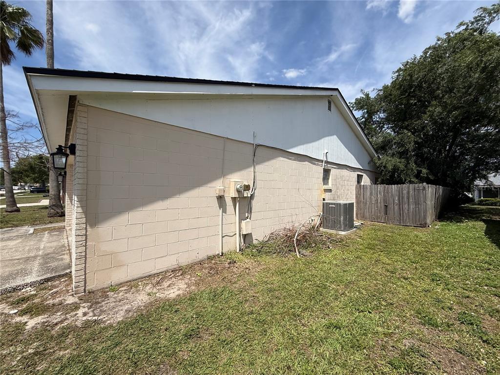 A side view of a beige concrete block house with an exterior air conditioning unit — 712 HAZY MEADOW COURT, BRANDON, FL