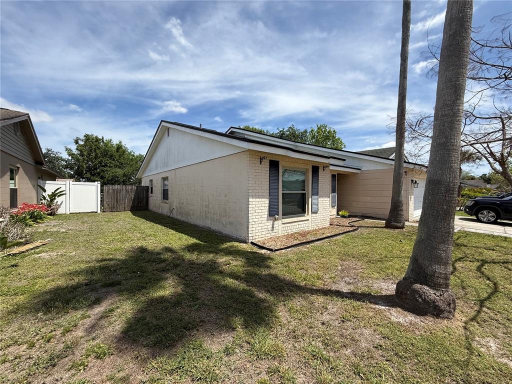 A side view of a single-story brick house with a lawn and palm trees — 712 HAZY MEADOW COURT, BRANDON, FL