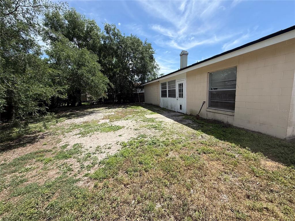 The exterior of a beige concrete block house features a backyard with sparse grass — 712 HAZY MEADOW COURT, BRANDON, FL
