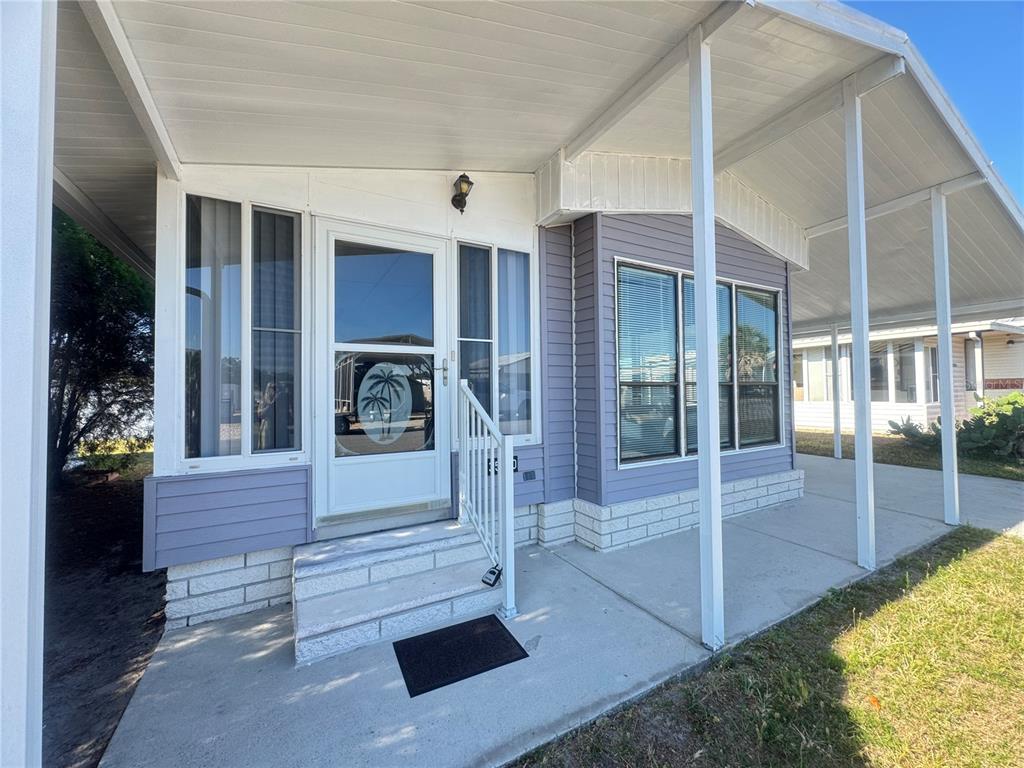 The exterior of a mobile home features a concrete porch, white railings, and purple siding — 35220 DODIE DRIVE UNIT 13, ZEPHYRHILLS, FL