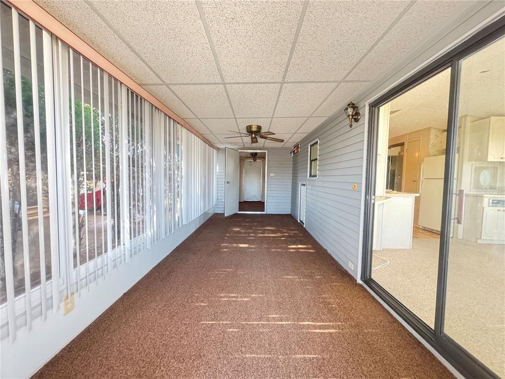A long, enclosed porch features brown carpeting, vertical blinds, and a ceiling fan — 35220 DODIE DRIVE UNIT 13, ZEPHYRHILLS, FL