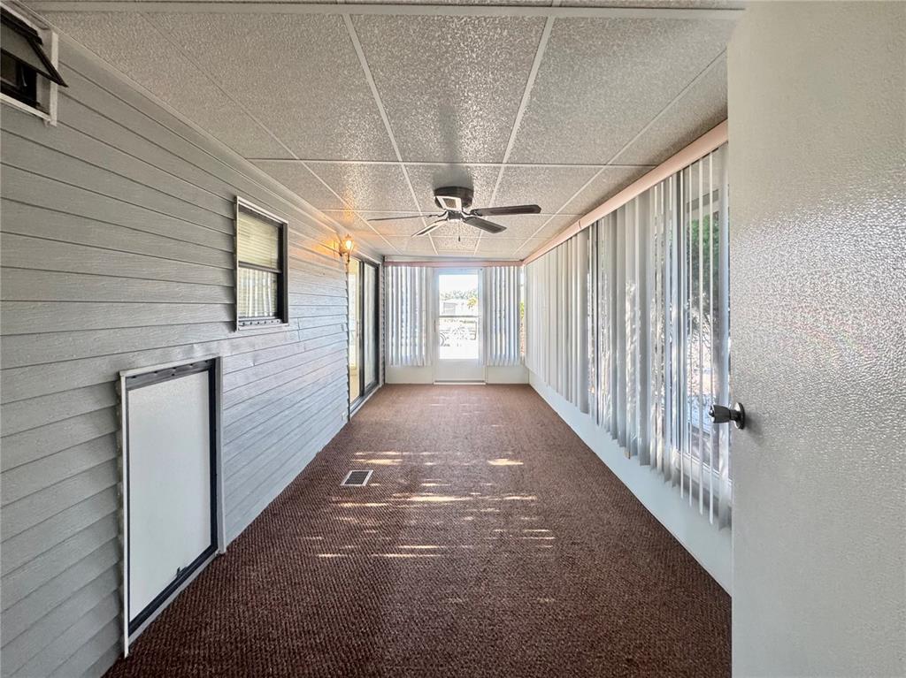 A long, enclosed porch features brown carpeting, gray horizontal siding, and a ceiling fan — 35220 DODIE DRIVE UNIT 13, ZEPHYRHILLS, FL
