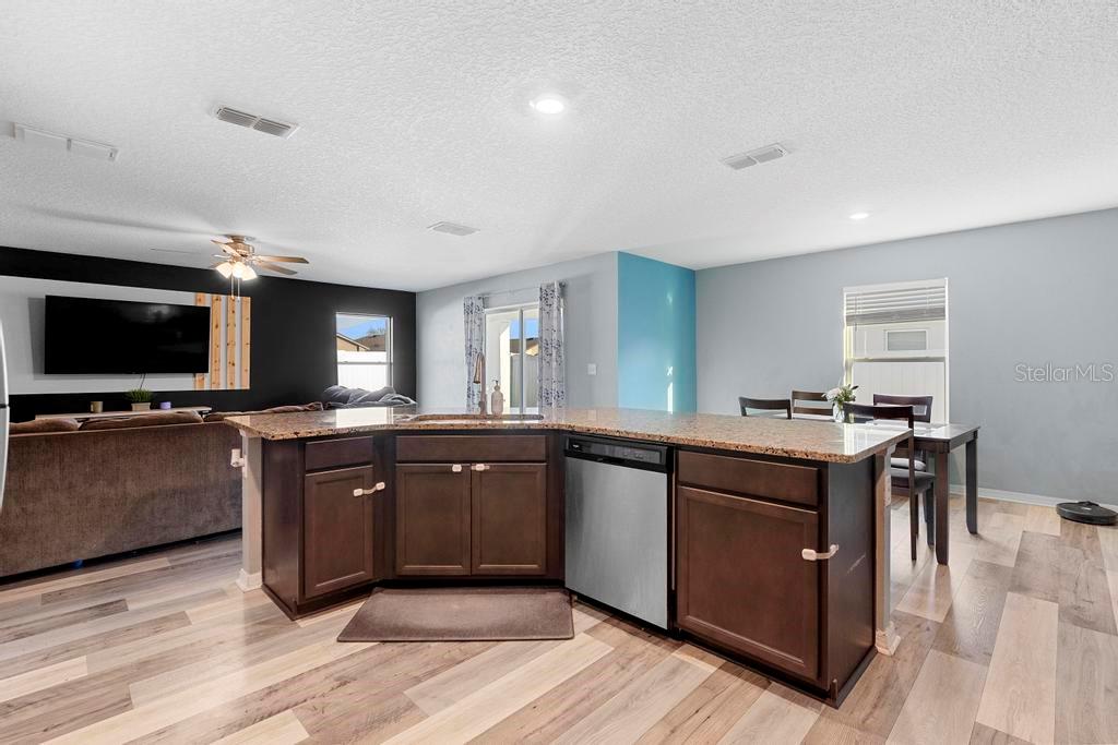 A kitchen island with dark wood cabinets and granite countertops sits before a living area — 440 KENSINGTON VIEW DRIVE, WINTER HAVEN, FL