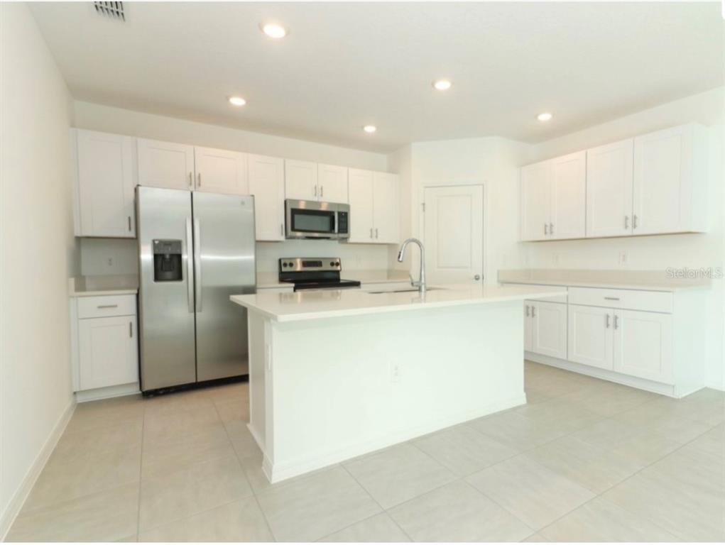 A modern kitchen features white cabinets, stainless steel appliances, and a central island with seating — 249 E ACORN RD, HAINES CITY, FL