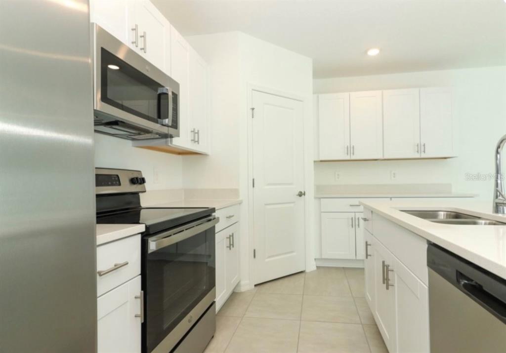 A kitchen with white cabinets, stainless steel appliances, quartz countertops, and light tile flooring — 249 E ACORN RD, HAINES CITY, FL