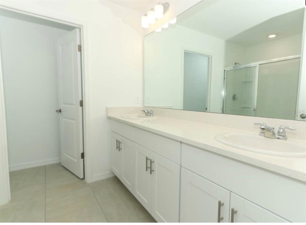 A bathroom features a white double vanity with a large mirror and tiled flooring — 249 E ACORN RD, HAINES CITY, FL