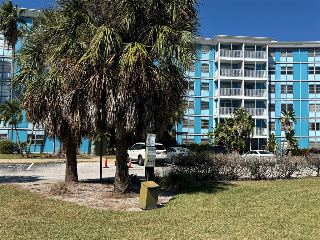 A multi-story blue apartment building stands behind a parking lot and palm trees — 3315 58TH AVENUE S UNIT 201, ST PETERSBURG, FL