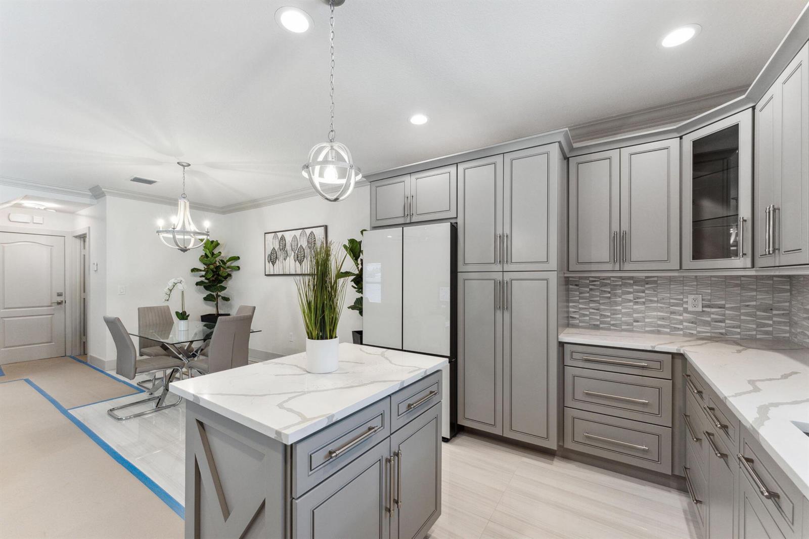 A modern kitchen features gray cabinets, a marble-topped island, and an adjacent dining area — 522 Lucky Lane, Delray Beach FL 33444, DELRAY BEACH, FL