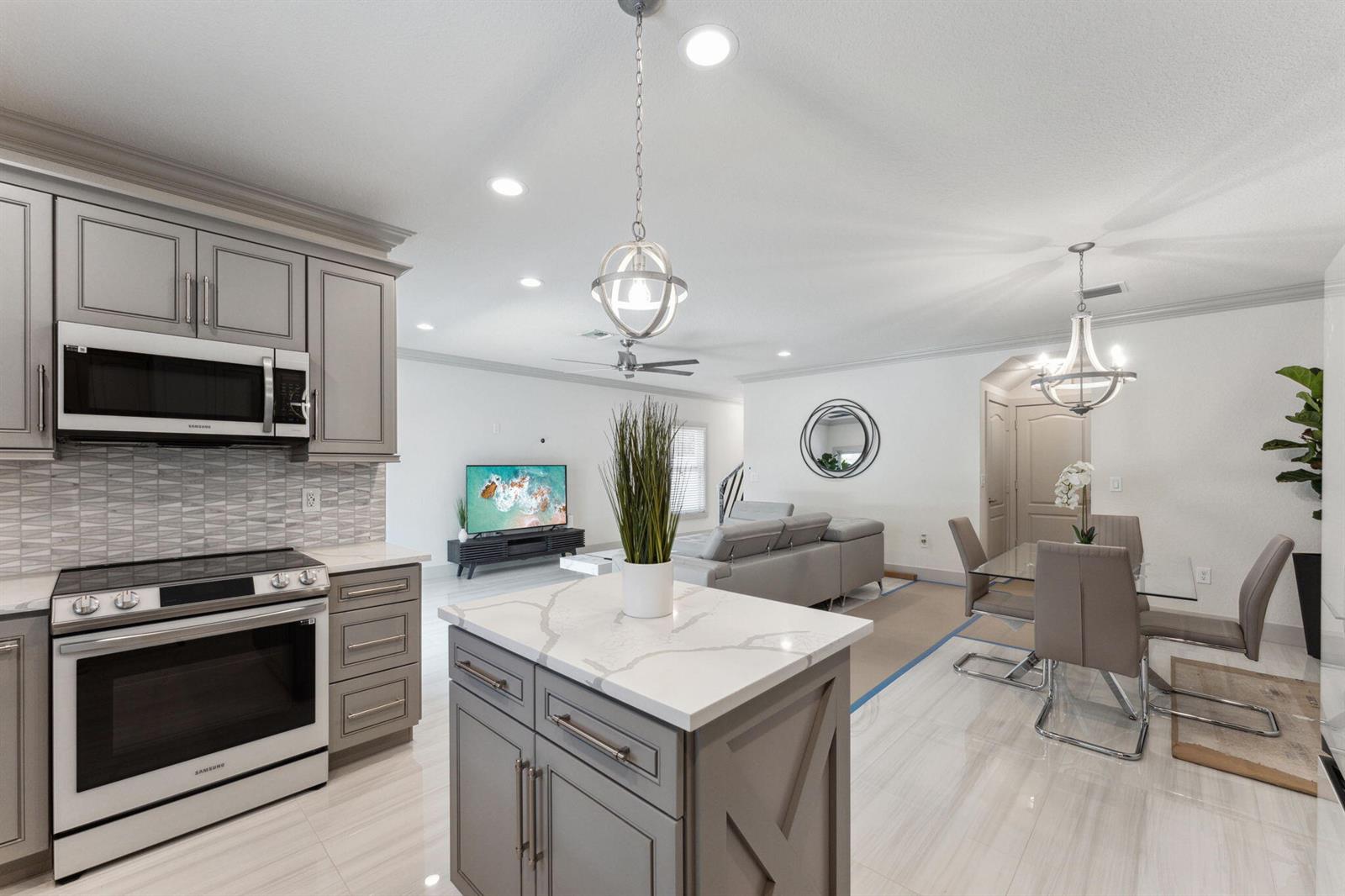 A kitchen with gray cabinets, a marble-topped island, and an open-concept dining and living area — 522 Lucky Lane, Delray Beach FL 33444, DELRAY BEACH, FL