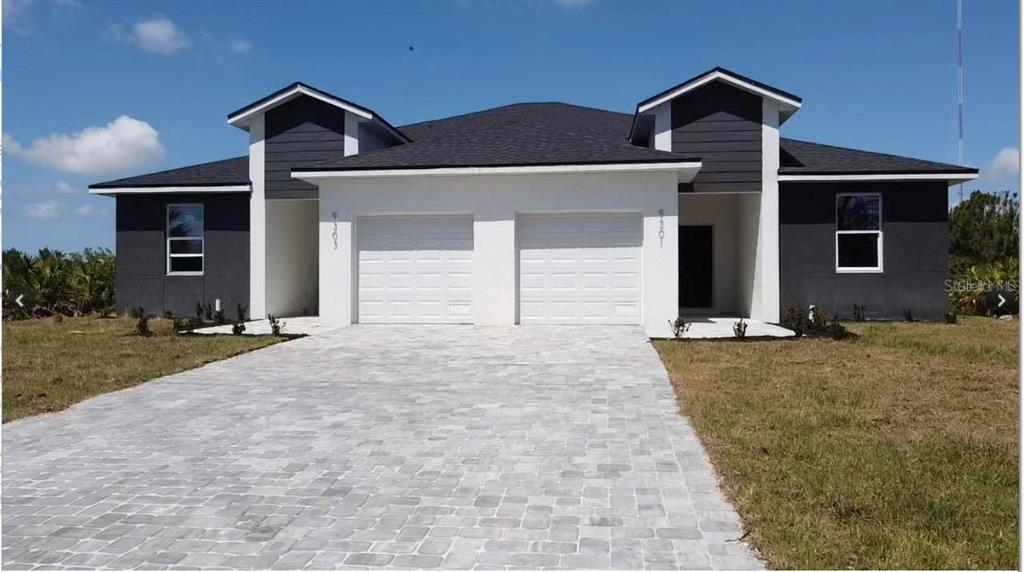 A modern duplex with dark gray siding, white stucco accents, and two attached garages — 10380 PORT EVERGLADES STREET, PORT CHARLOTTE, FL