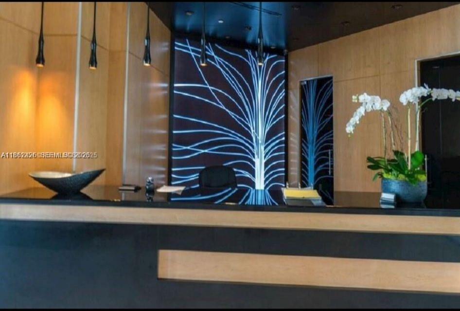 A modern reception desk features a black countertop, wood paneling, and a glowing tree-patterned backdrop — 901 Brickell Key Blvd # 2701, Miami FL 33131, MIAMI, FL