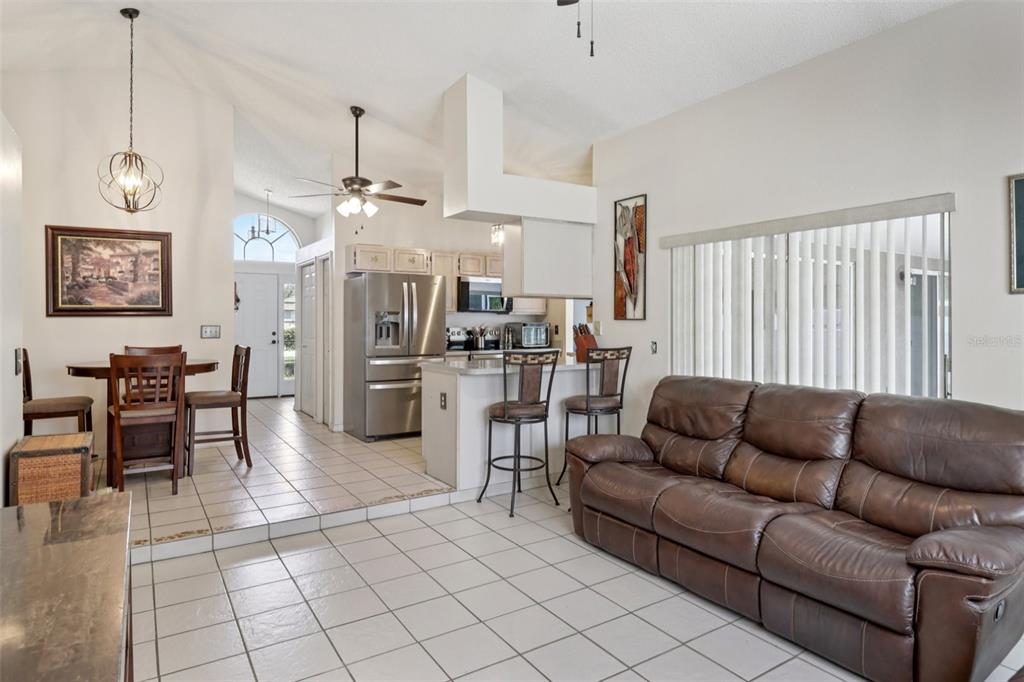 An open-concept living room and kitchen featuring tile flooring, a brown sofa, and bar seating — 1977 S OLD MILL DRIVE, DELTONA, FL