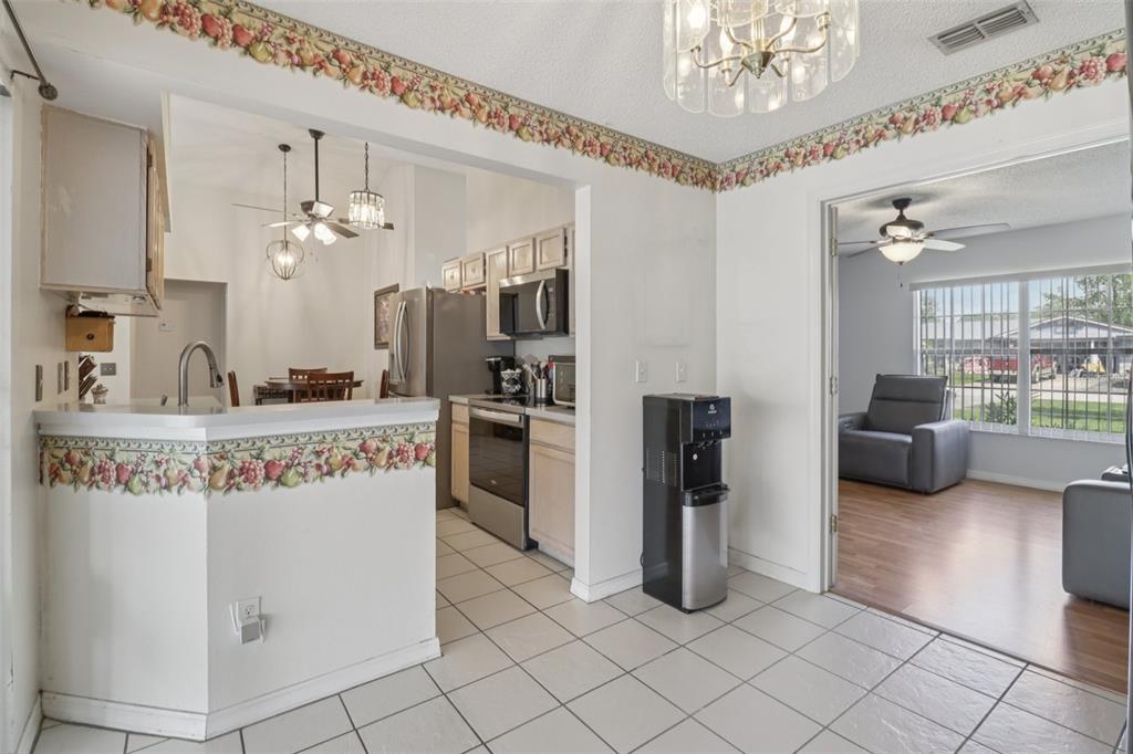 A kitchen with tile floors, stainless steel appliances, and a fruit-patterned wallpaper border — 1977 S OLD MILL DRIVE, DELTONA, FL